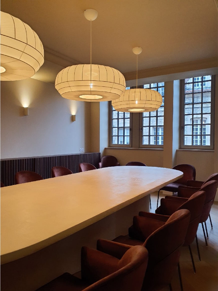 Salle de réunion avec longue table claire, fauteuils en velours et suspensions en papier