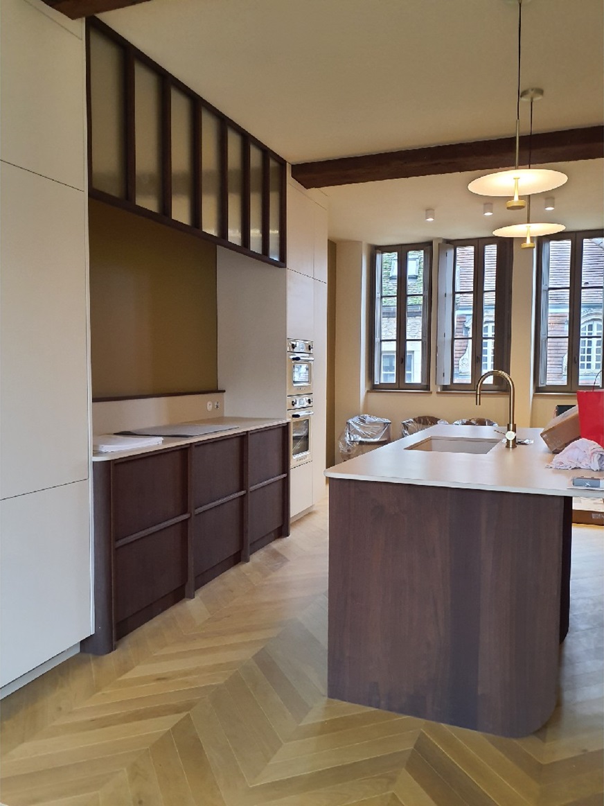 Cuisine aux façades en bois sombre avec îlot central, verrière d'atelier et parquet en point de Hongrie