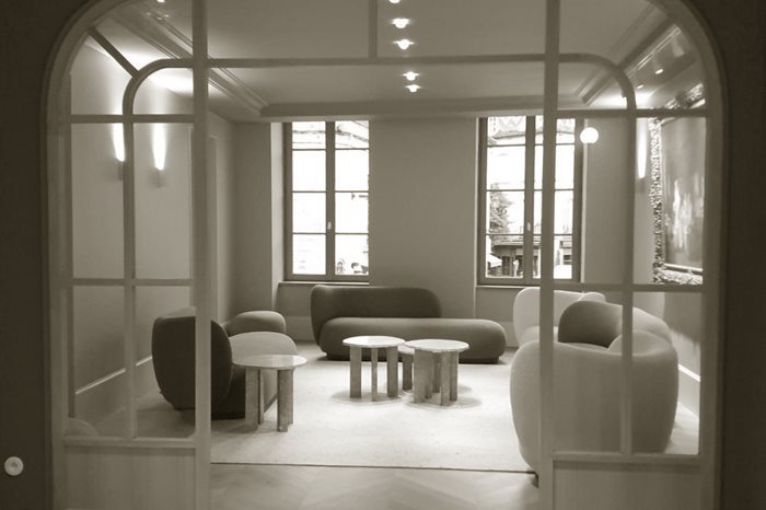 Salon vu à travers une verrière cintrée en bois clair, avec canapés arrondis et tables basses en pierre rose